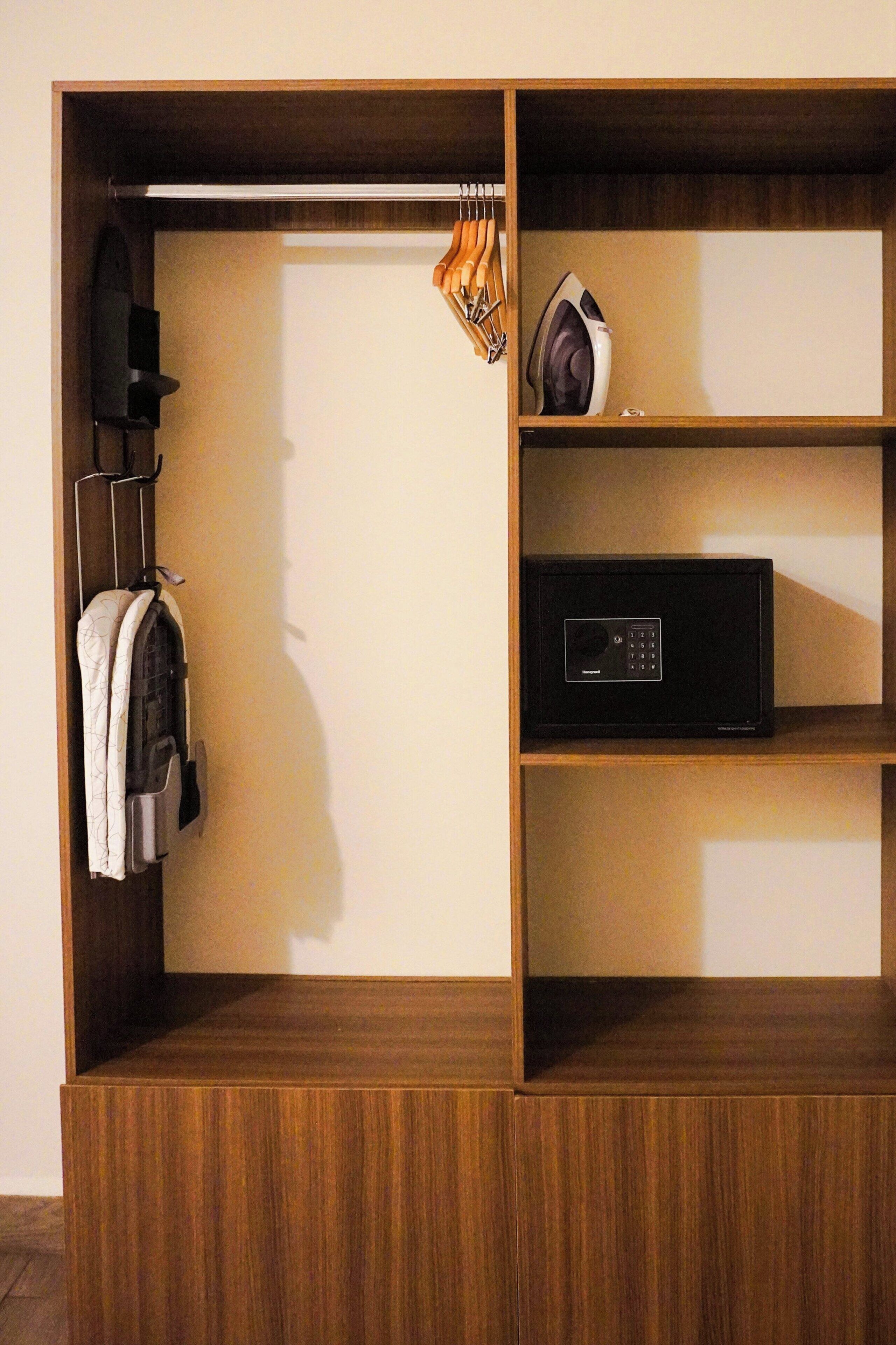 A wooden wardrobe with a hanging rack, a microwave, and a shelf with a remote control.