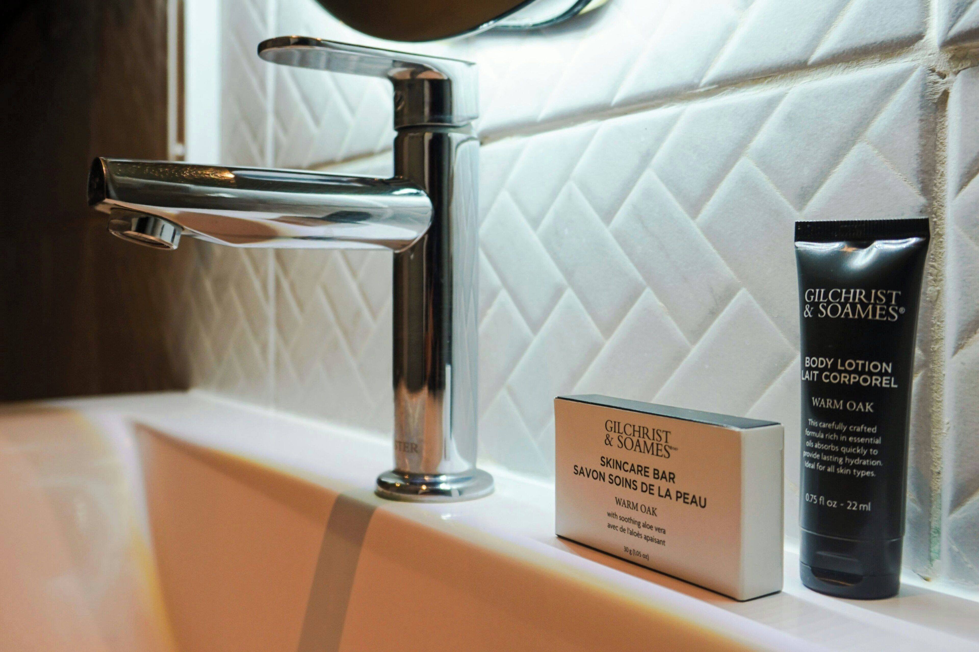 A bathroom sink with a modern faucet, a Gilchrist & Soames skincare bar, and a body lotion tube.