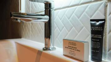 A bathroom sink with a modern faucet, a Gilchrist & Soames skincare bar, and a body lotion tube.