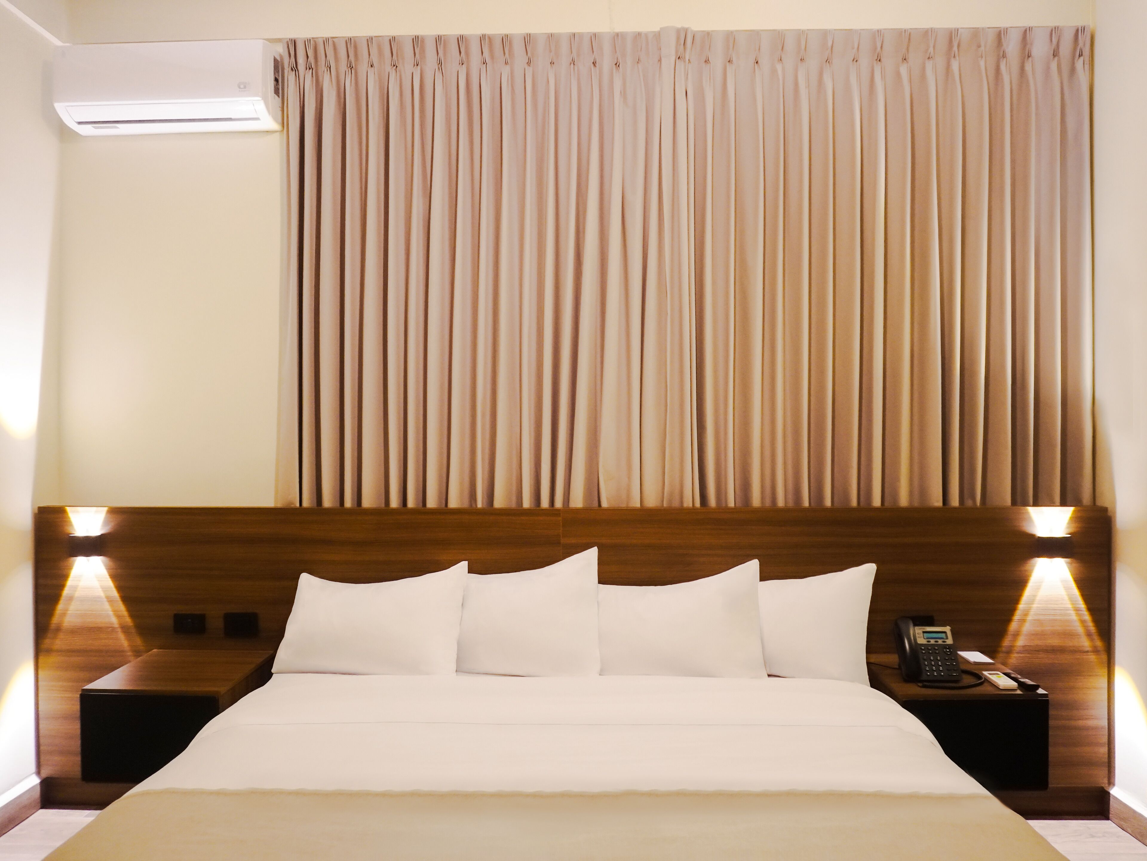 A hotel room with a large bed, two bedside tables with lamps, a wooden headboard, and a curtain.