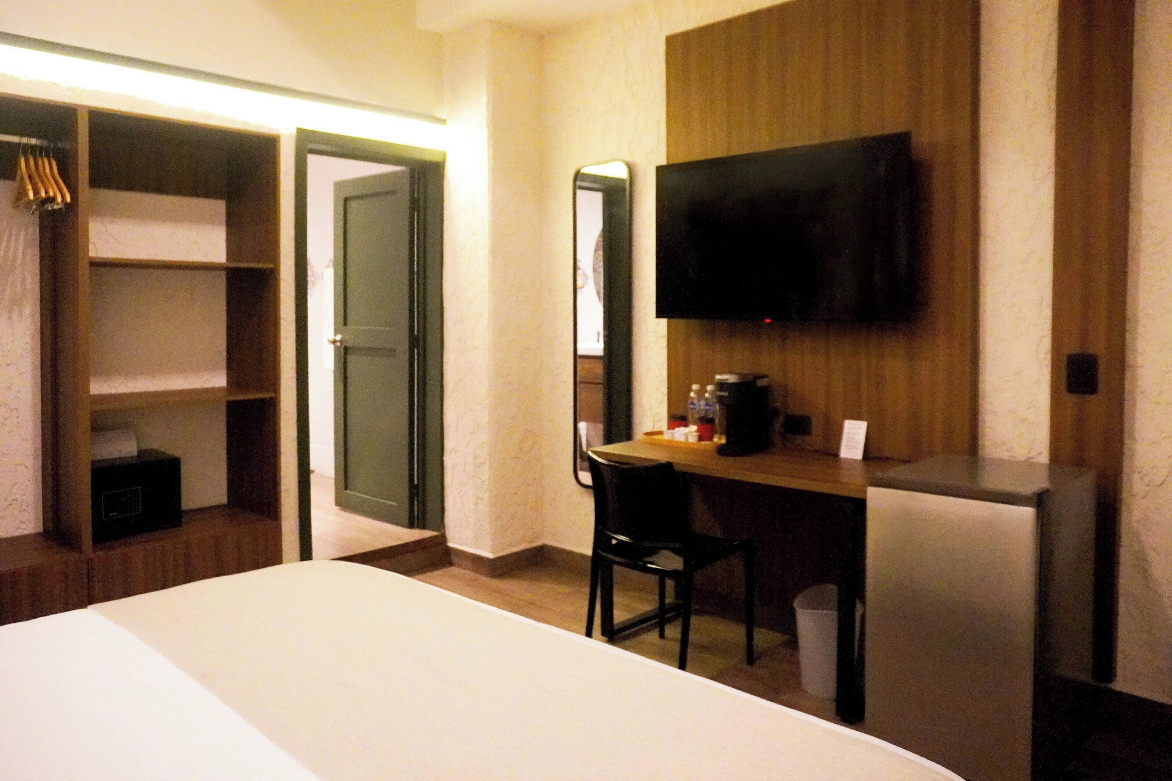 A hotel room with a bed, a desk, a chair, a television, and a wardrobe.