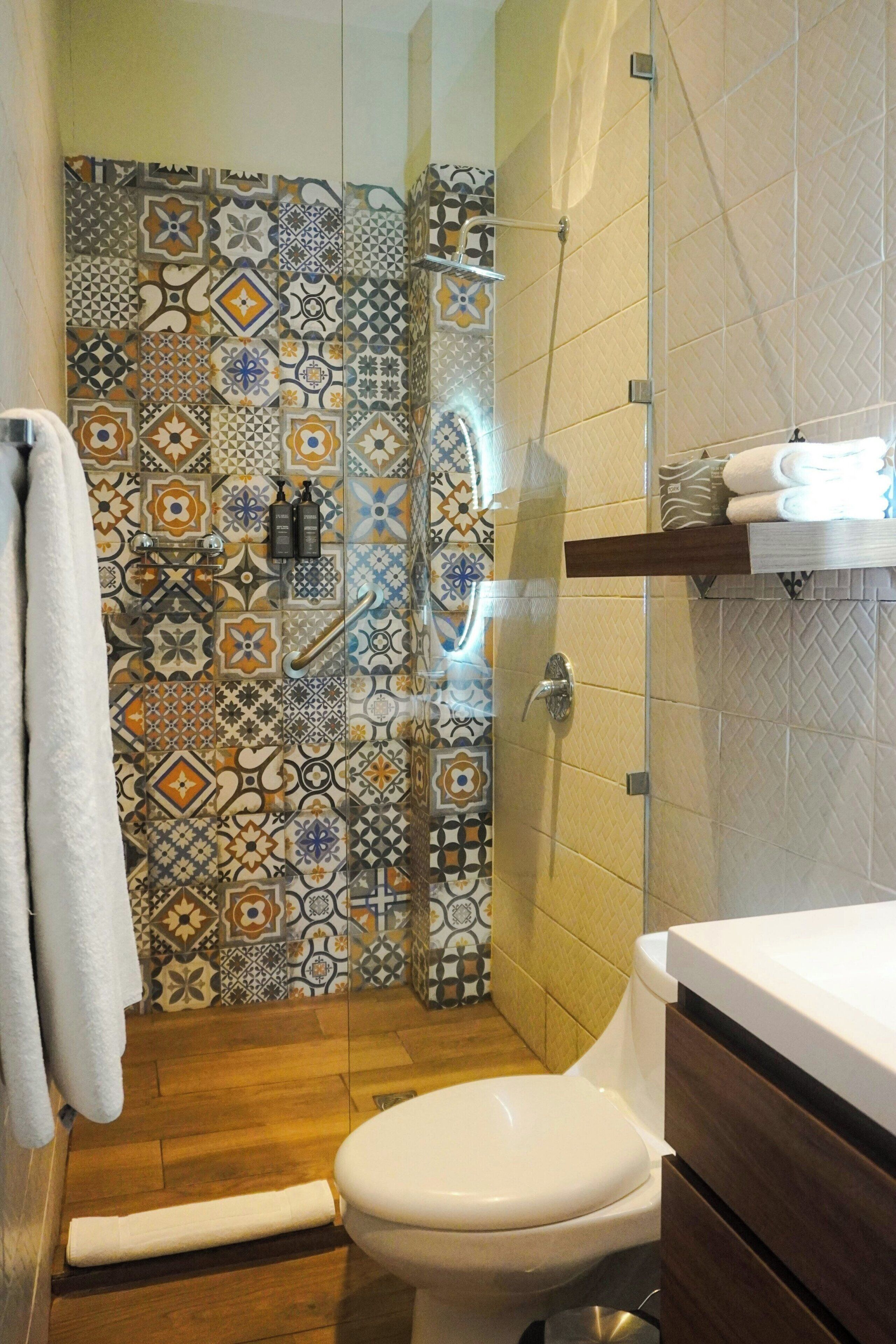 Un baño con pared de ducha enlosada, inodoro y piso de madera.
