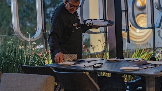 Un uomo seduto a un tavolo con una parete divisoria in vetro, un cartellino identificativo e un menu.