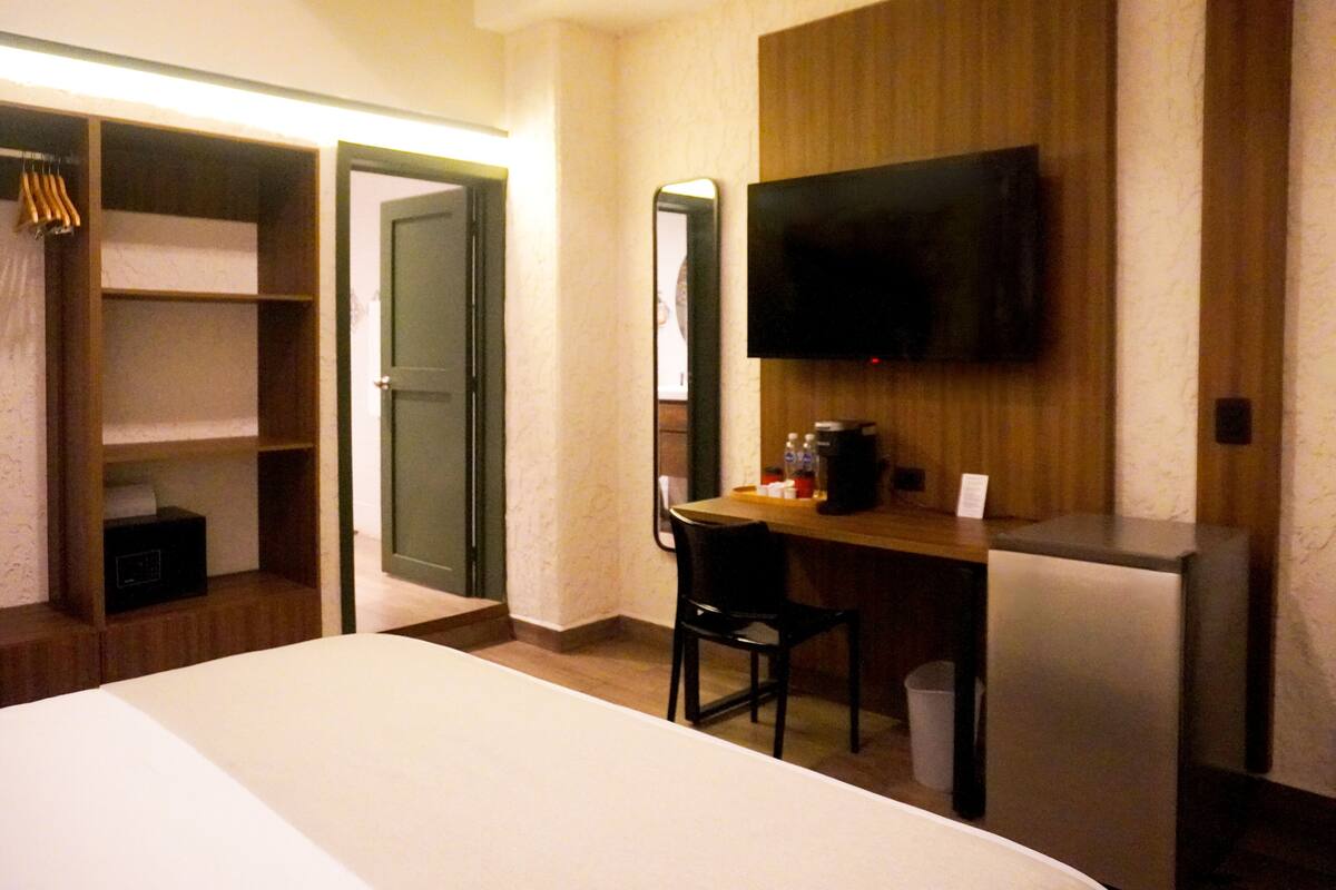 Une chambre d’hôtel comprenant un lit, un bureau avec une chaise, un téléviseur fixé au mur et une armoire.