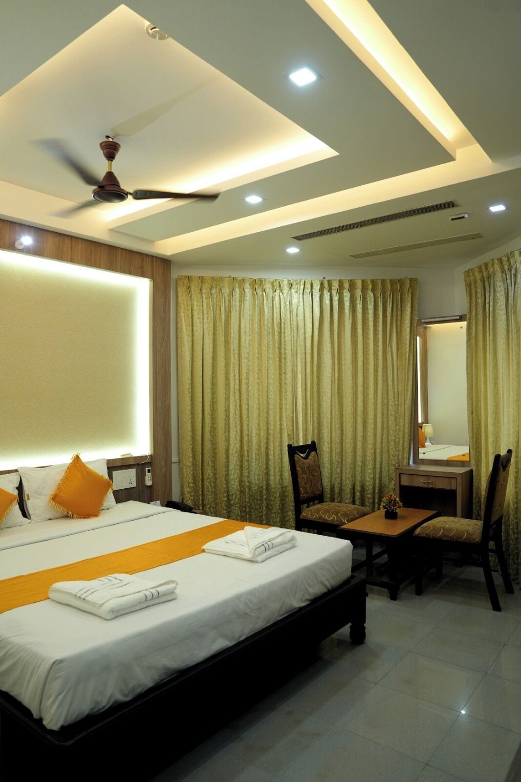 A hotel room with a large bed, a desk, a chair, a ceiling fan, and curtains.