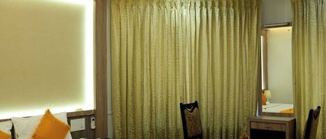 A hotel room with a large bed, a desk, a chair, a ceiling fan, and curtains.