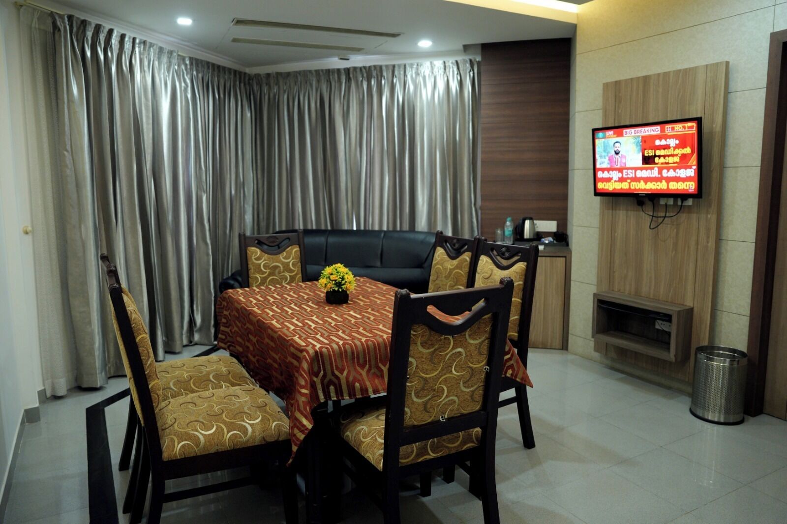 A dining area with a table set for four, a sofa, and a television mounted on the wall.