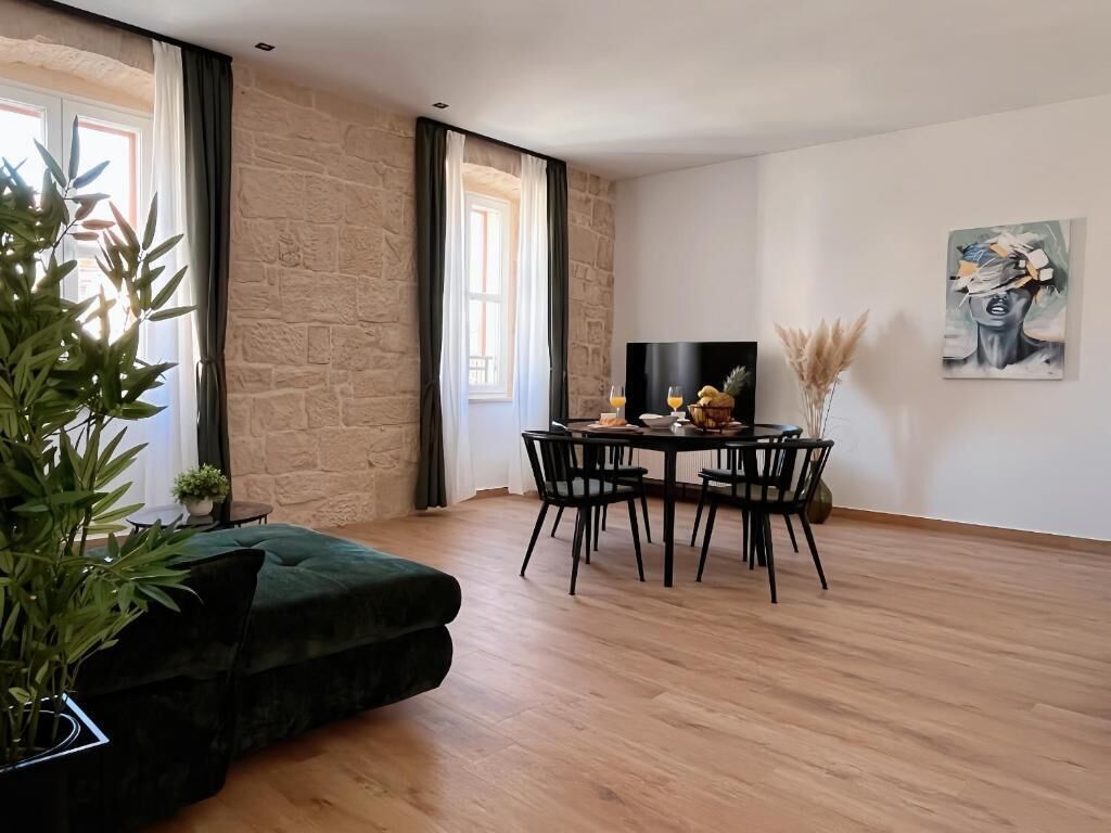 A modern living room with a stone wall, a green sofa, a dining table with chairs, and a painting on the wall.