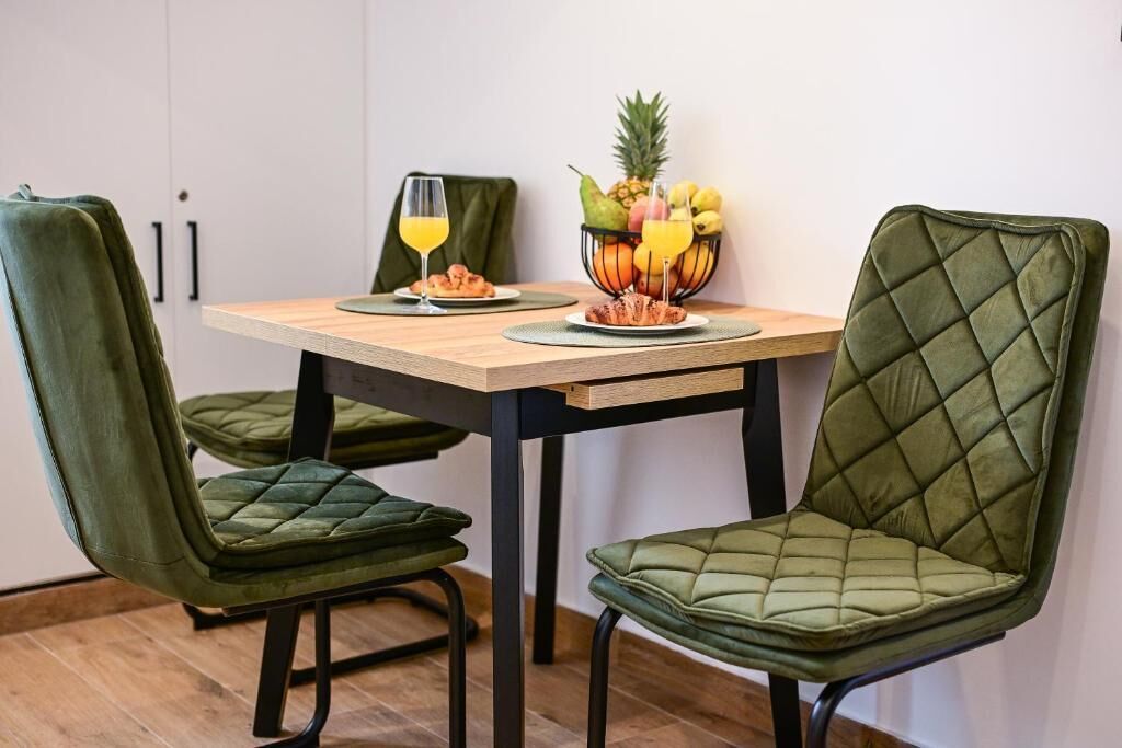 En matplats med ett träbord, två gröna stolar med vaddering, en fruktskål och ett glas apelsinjuice.