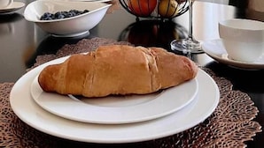 Ein Frühstückstisch mit Croissants, Früchten und Orangensaft, ein Bild an der Wand und ein Fenster mit Vorhängen.
