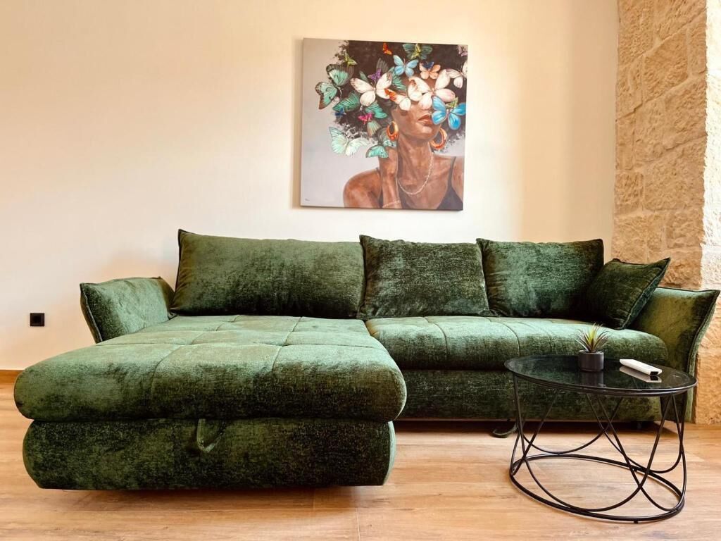 A green sectional sofa with a matching ottoman, a small round table with a plant, and a painting on the wall.