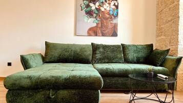 A green sectional sofa with a matching ottoman, a small round table with a plant, and a painting on the wall.