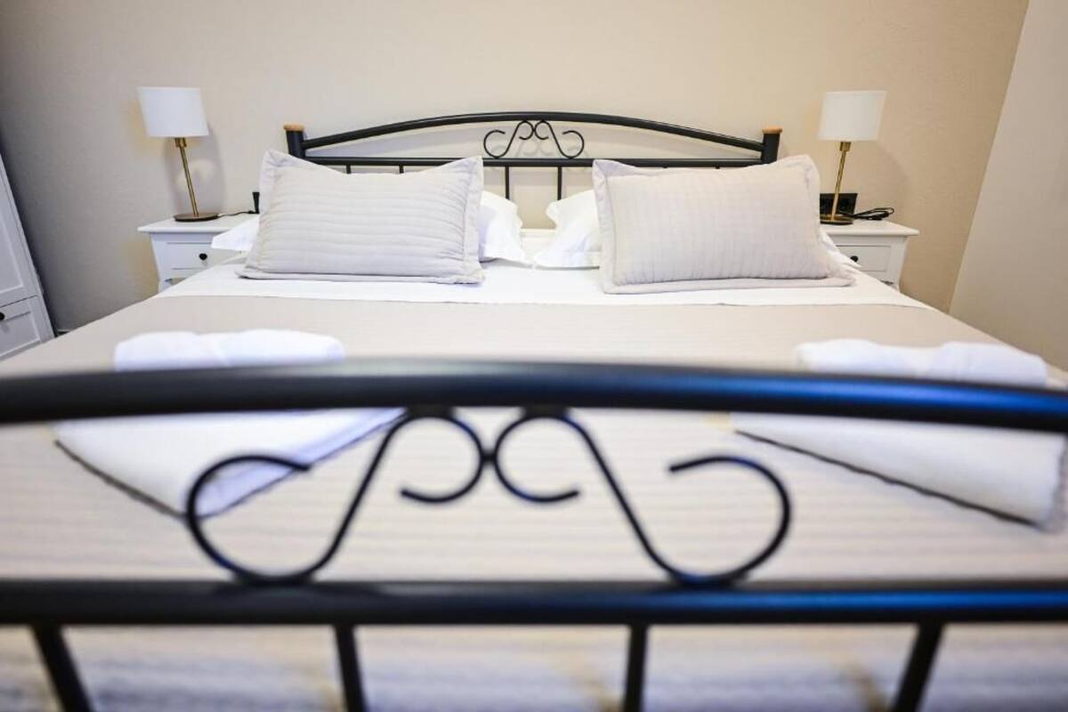 Un lit bien fait, avec du linge de lit blanc et des oreillers, une tête de lit en métal noir et deux tables de chevet avec des lampes.