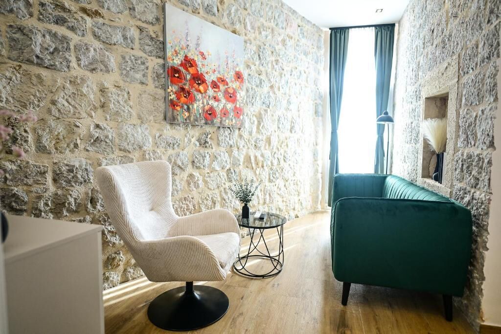 A room with a stone wall, a white armchair, a green sofa, and a painting of red flowers.