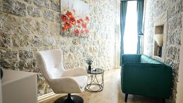 A room with a stone wall, a white armchair, a green sofa, and a painting of red flowers.