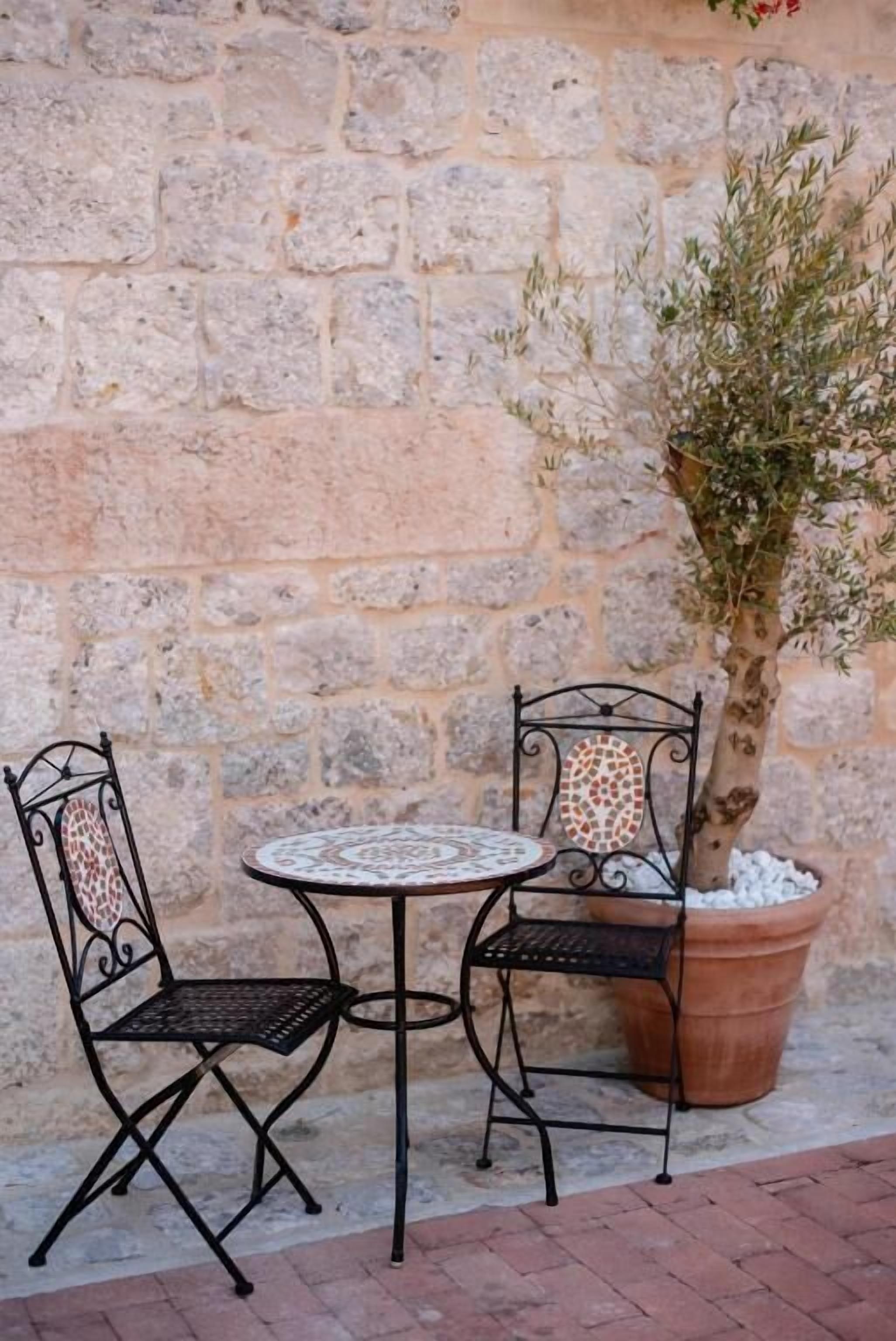 A stone wall, two metal chairs, a round table, and a potted tree.