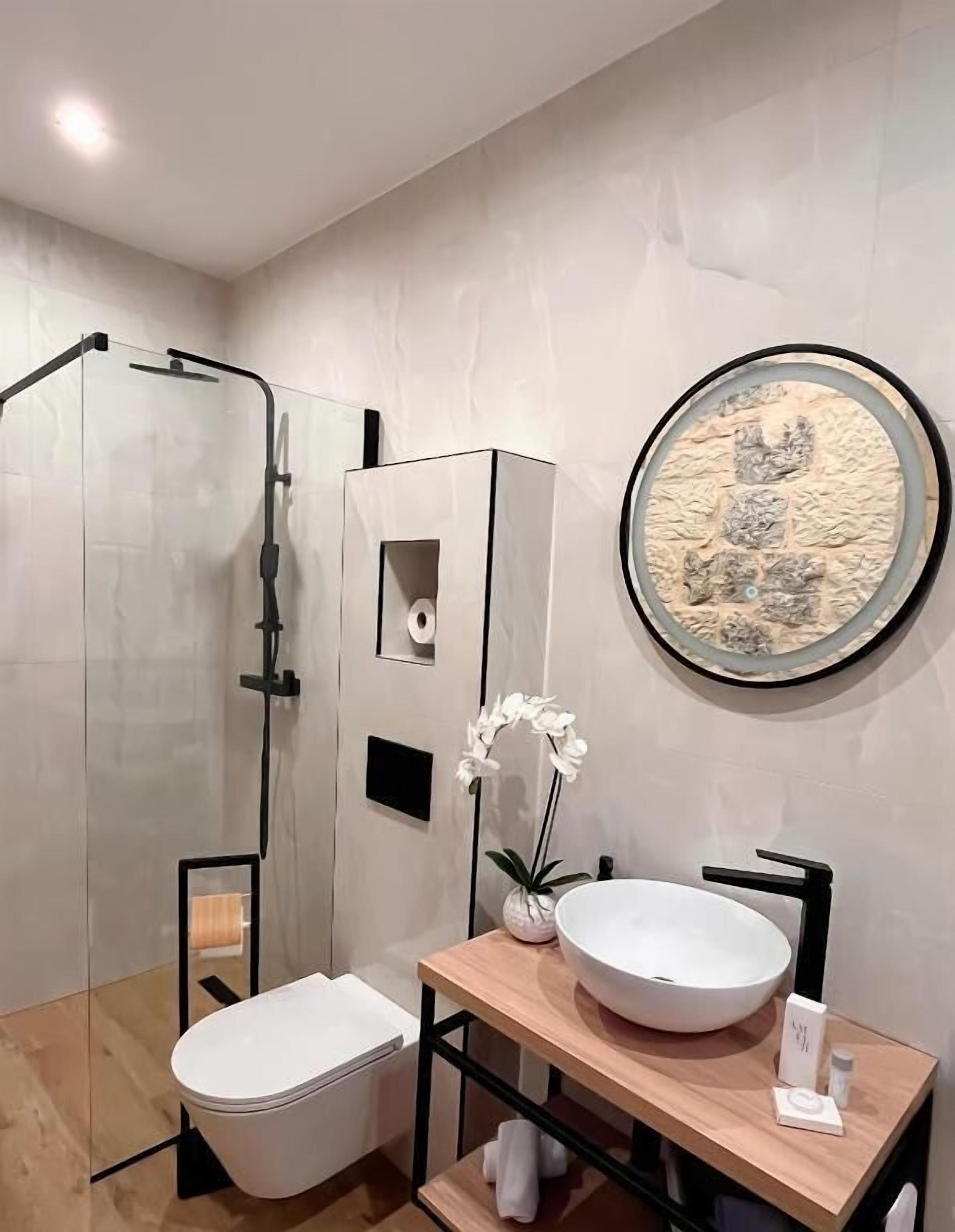 Un baño moderno con ducha envuelta en vidrio, inodoro blanco, tocador con un lavamanos grande y un adorno en la pared.