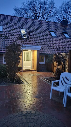 A house with a tiled roof, a front door, and a white plastic chair in the driveway.