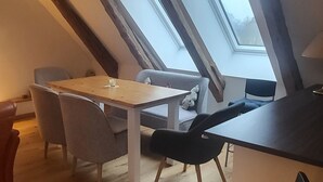 Tunnelmallinen parvi-makuuhuone, jossa on kalteva katto, kattovalokuviot, puinen ruokapöytä ja modernit huonekalut.