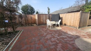 A patio with a brick floor, two white plastic chairs, and a table. - Comfortable Owl's Nest Vacation Rental (Bad Zwischenahn)