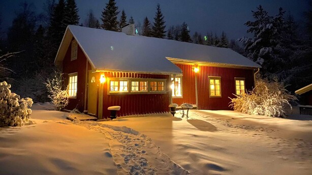 Una casa cubierta de nieve con techo inclinado y varias ventanas, rodeada de árboles cargados de nieve.
