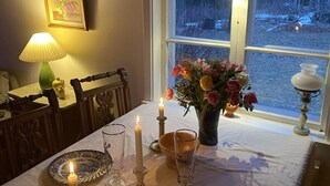 Un comedor acogedor con una mesa lista para dos, que incluye una vela, un jarrón de flores y una lámpara.