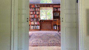 Una habitación con una amplia estantería, un tapiz decorativo y vistas al exterior a través de una ventana.
