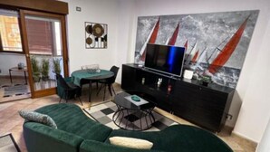Ett modernt vardagsrum med en böjd, grön soffa, ett matbord med stolar, en svart möbel för underhållningssystem med en platt-tv och en stor, abstrakt målning på väggen.