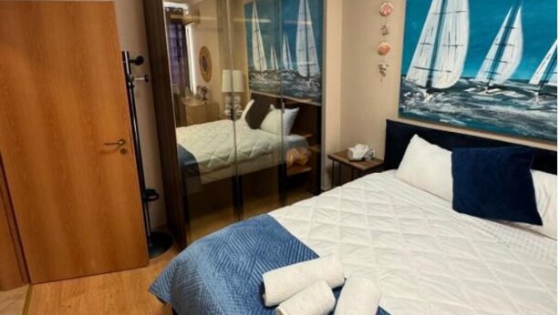 Ett hotellrum med en säng, en spegel, en målning som föreställer segelbåtar och en garderob i trä.