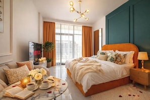 A modern hotel room with a large bed, a TV, a coffee table with a book and a cup, and a view of the city through the window. - Luxury Studio with Pool and Parking (Dubai)