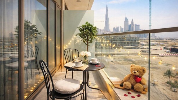 A balcony with a table, chairs, a teddy bear, and a city view. - Luxury Studio with Pool and Parking (Dubai)