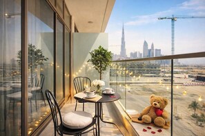 A balcony with a table, chairs, a teddy bear, and a city view. - Luxury Studio with Pool and Parking (Dubai)