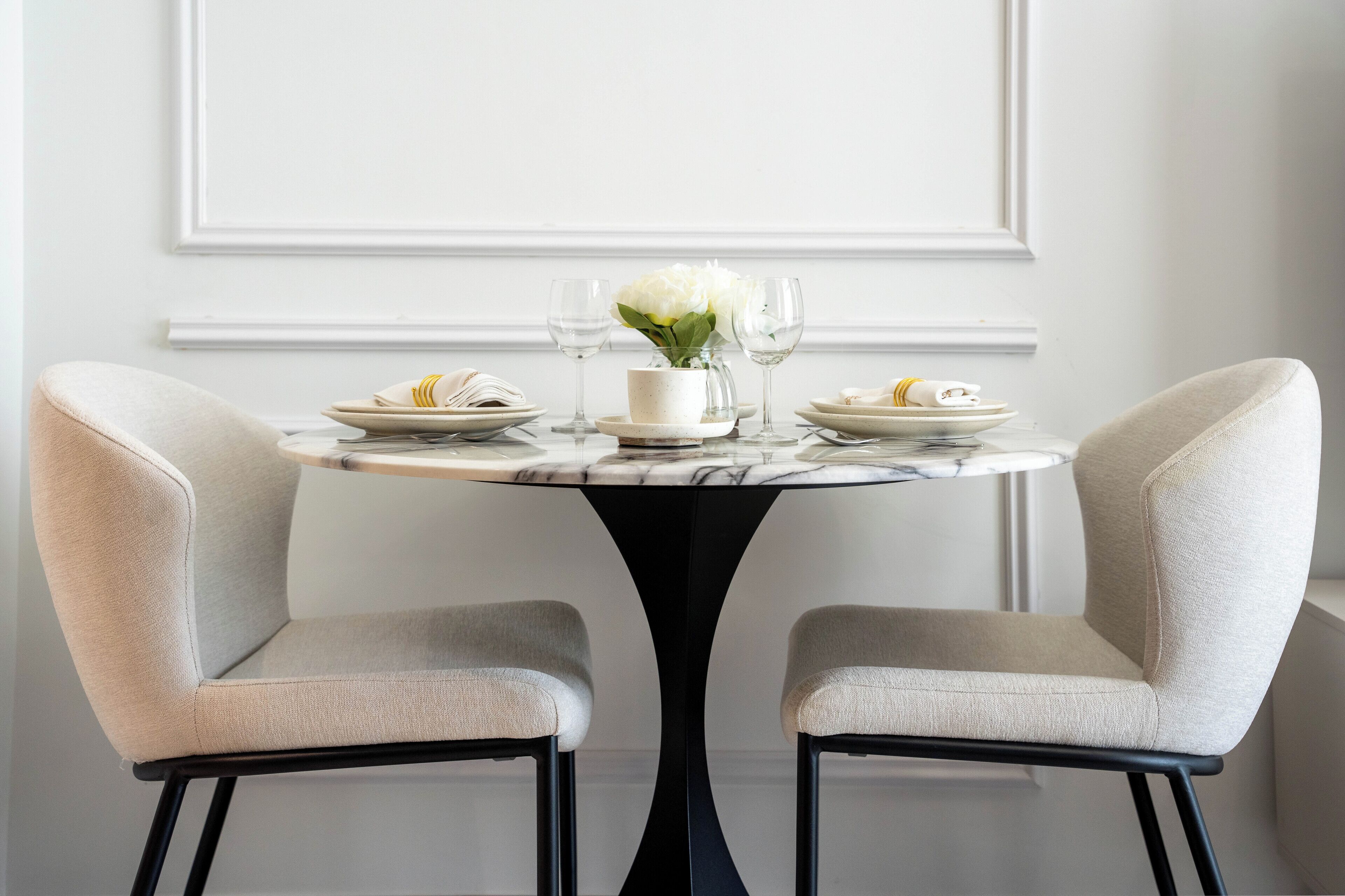 A dining table with two chairs, a vase with flowers, and plates and glasses.