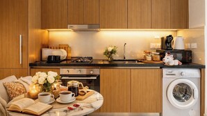 A compact kitchen with wooden cabinets, a gas stove, a coffee maker, and a washing machine. - Luxury Studio with Pool and Parking (Dubai)