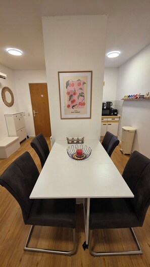 A dining area with a white table, black chairs, a framed picture of cherries, and a small fruit stand with glasses. - Exclusive complete apartment for 6 people (Groß-Gerau)