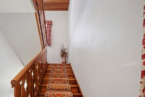 Eine Holztreppe mit gemusterten Teppichläufern, einer Vase mit Blumen und einem roten und weißen Vorhang mit Muster.