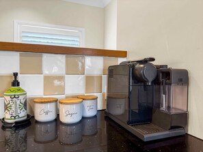 Une cuisine équipée d’une machine à café, d’un pot de crème à café et de trois bocaux à épices étiquetés « café », « sucre » et « thé ».