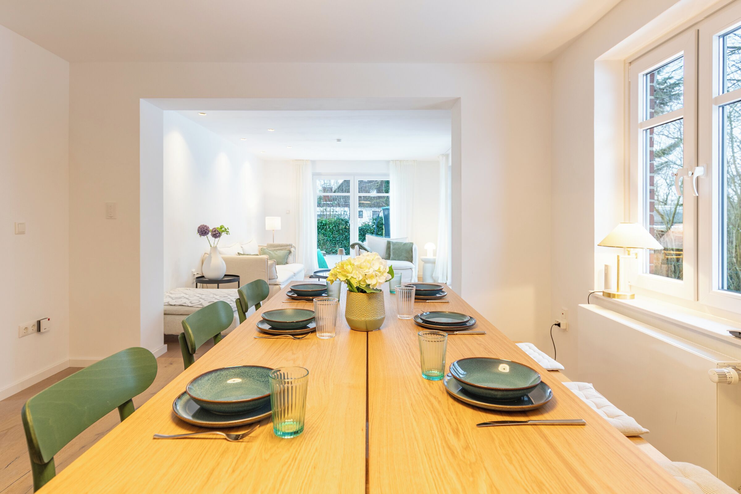 Ein Esszimmer mit einem Holztisch, gedeckt für sechs Personen, Stühlen und einer Blumenvase.