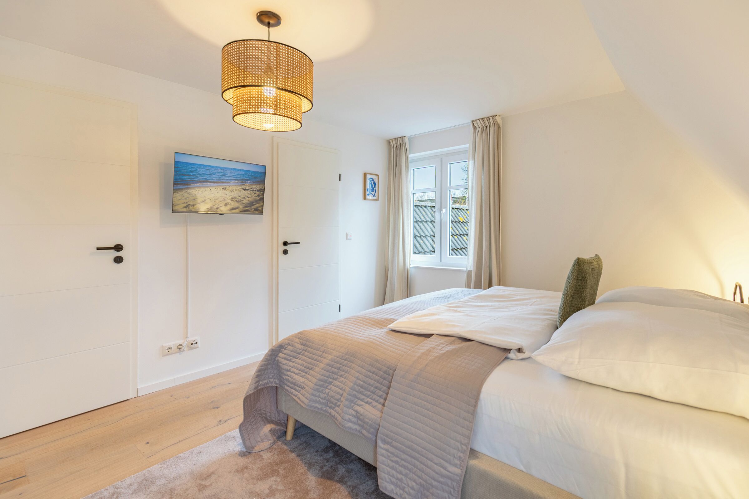A bedroom with a bed, a window with curtains, a painting on the wall, and a ceiling light fixture.