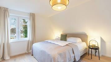 Ein Schlafzimmer mit einem Bett, einem Nachttisch mit Lampe, einem Fenster mit Vorhängen und einer Pendelleuchte.