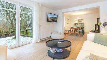 Ein modernes Wohnzimmer mit großem Fenster, einem runden schwarzen Tisch, einem weißen Sofa und einem Essbereich mit Holztisch und Stühlen.