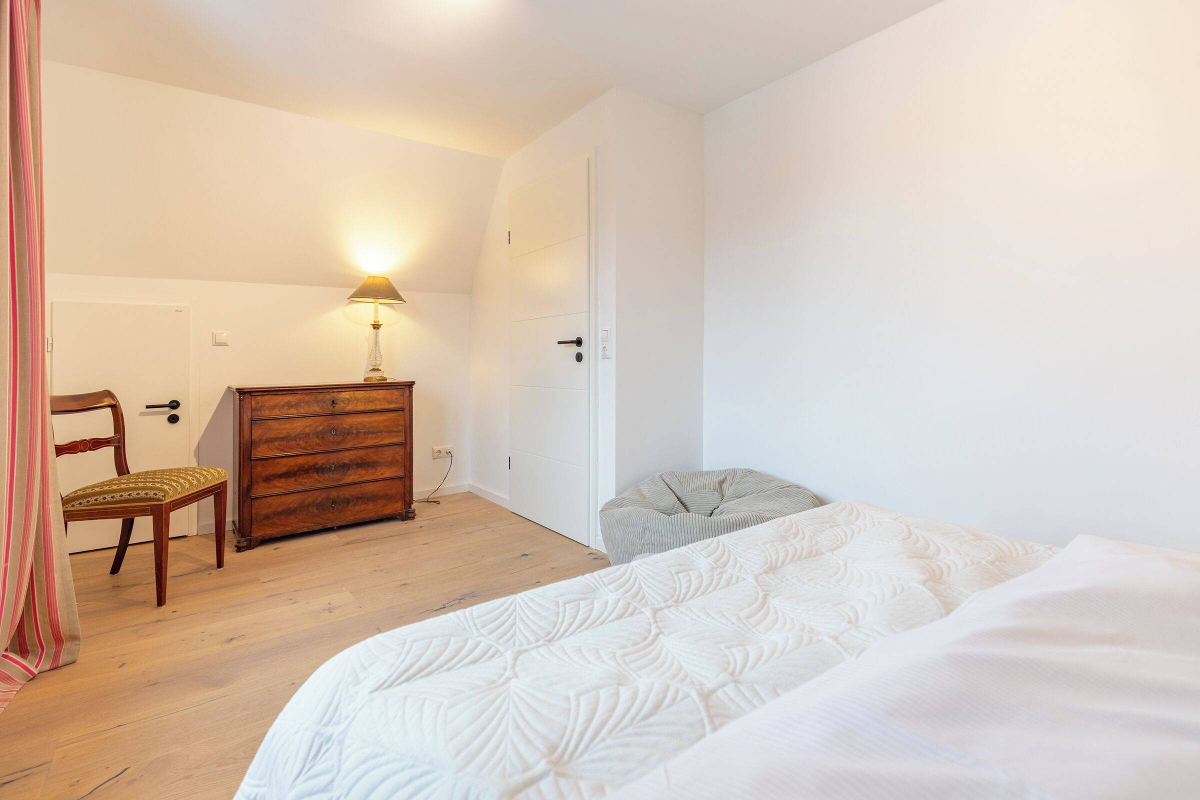 Ein Schlafzimmer mit einem Bett, einem Holzschrank, einem Stuhl und einer Lampe.