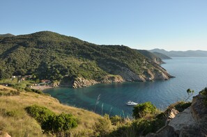 A coastal landscape with a boat on the water, a beach, and a hillside with vegetation. - Beachfront apartment, terrace with ocean view, parking, air conditioning (Toscana)