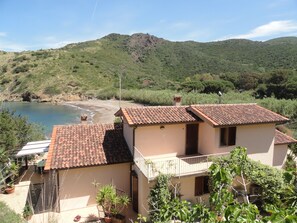 Ein Küstenanwesen mit einem Ziegeldach, einem Balkon und Blick auf das Meer und die Hügel.