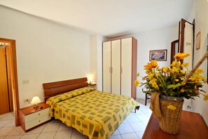 Ein Schlafzimmer mit Bett, Nachttisch, Kommode, Kleiderschrank und einer Vase mit Blumen.