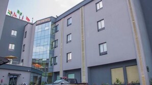 A modern hotel building with a glass facade, multiple windows, and a parking area with a few vehicles. - Henods Luxury  Suites (Lagos)