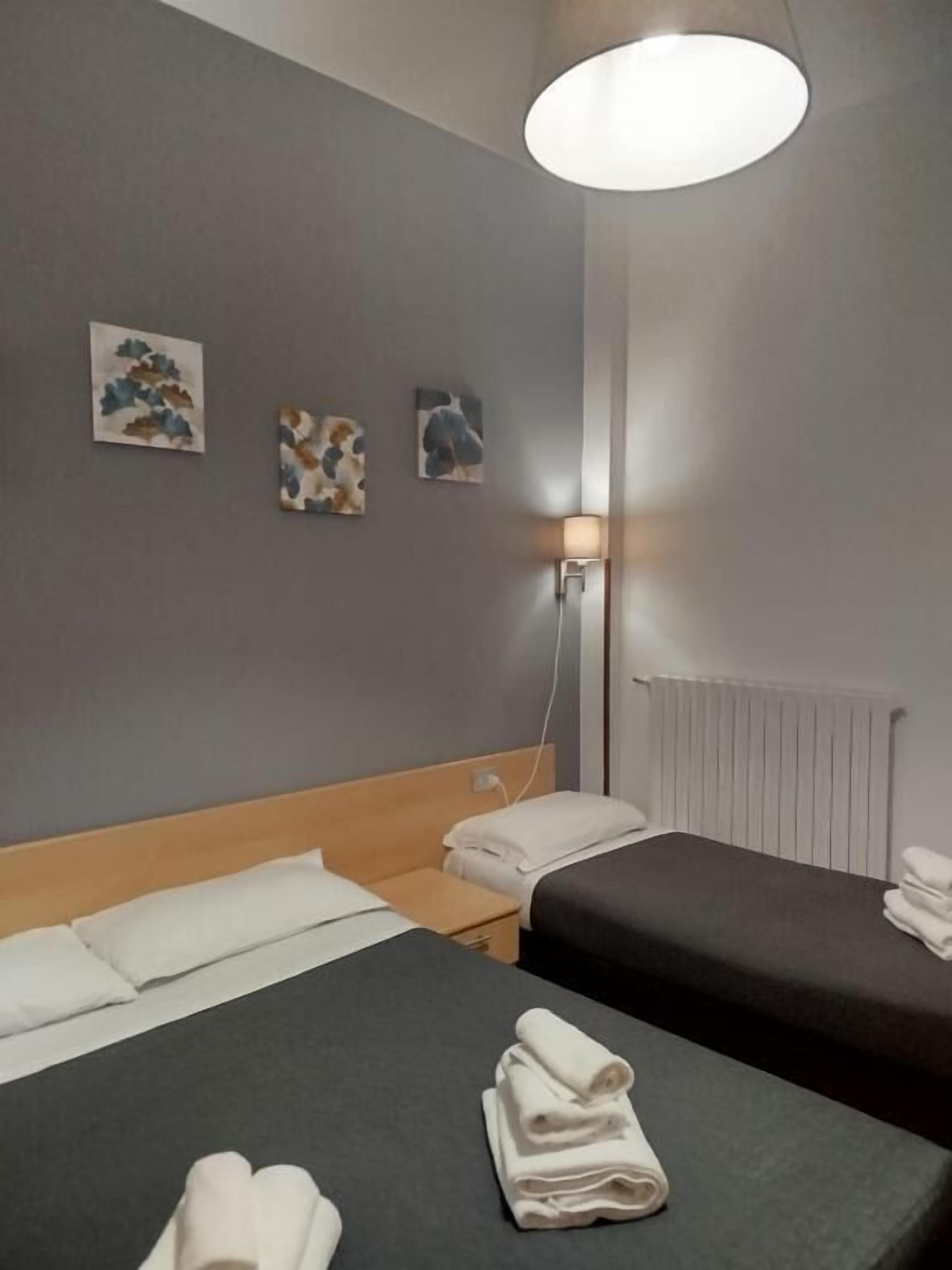 A hotel room with two beds, a bedside table, a lamp, and artwork on the wall.