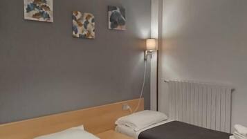 A hotel room with two beds, a bedside table, a lamp, and artwork on the wall.