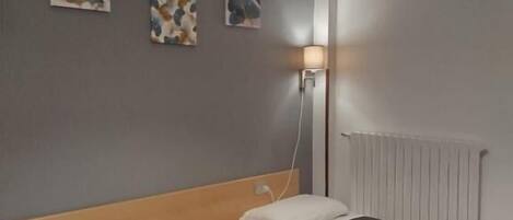 A hotel room with two beds, a bedside table, a lamp, and artwork on the wall.
