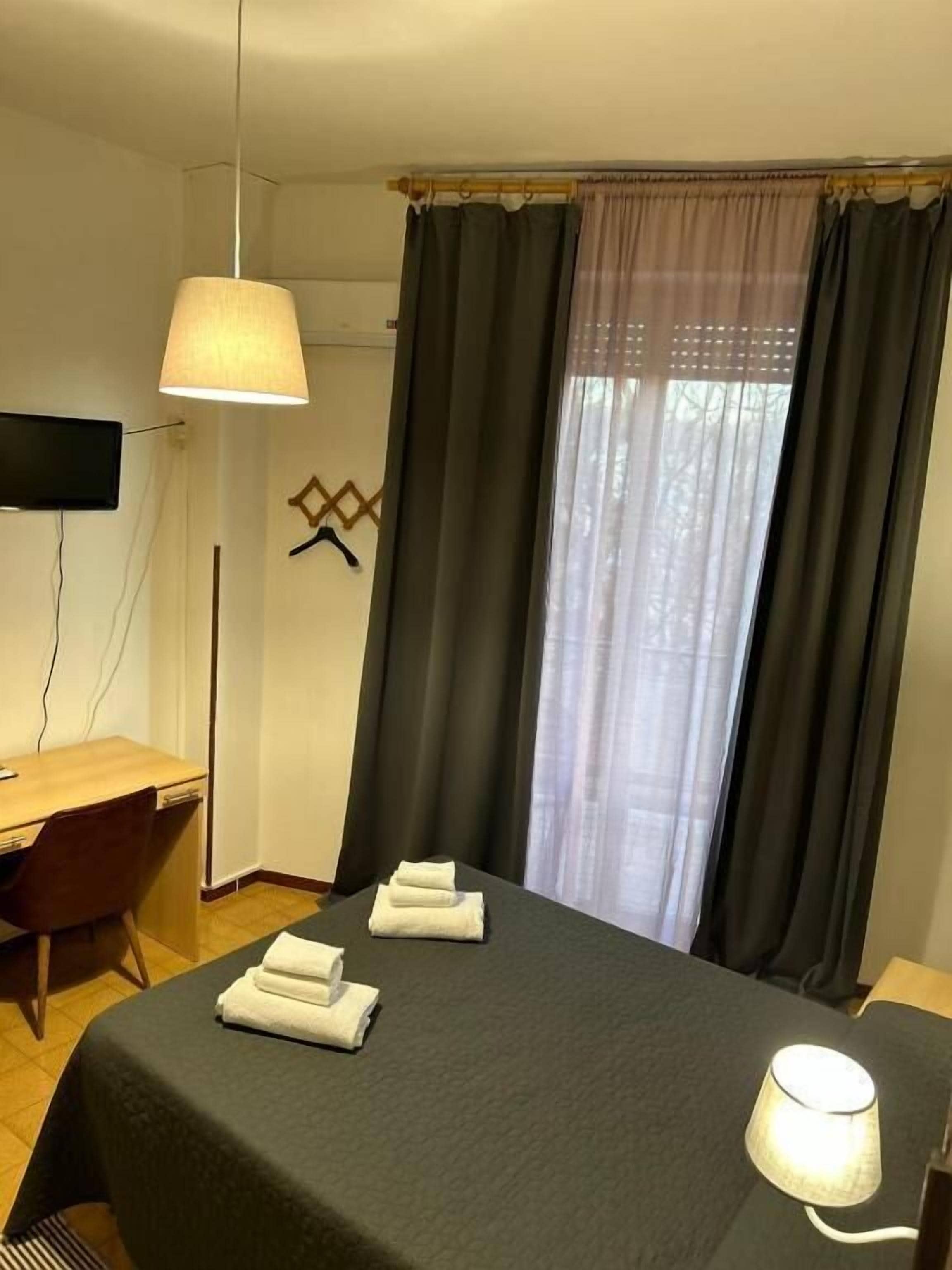 A hotel room with a bed, a desk, a chair, a TV, and a window with curtains.